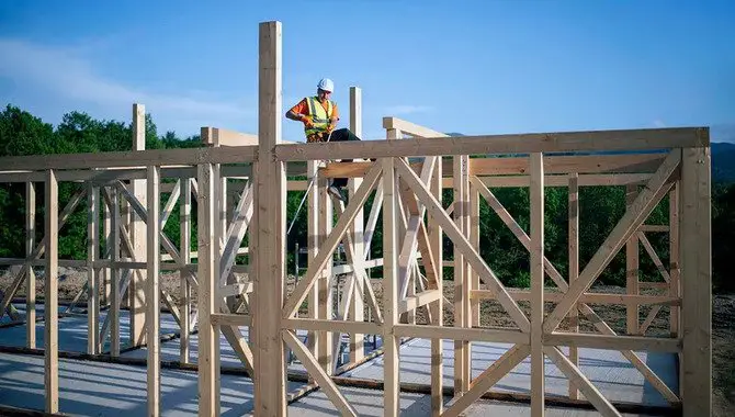 Builder working on rooftop frame of wooden construction building.
